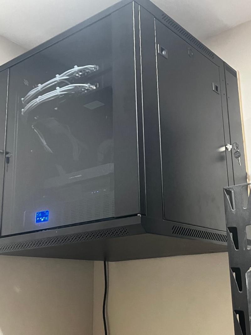 Locked wall-mounted network cabinet with glass door holding switches, recorder and battery backup