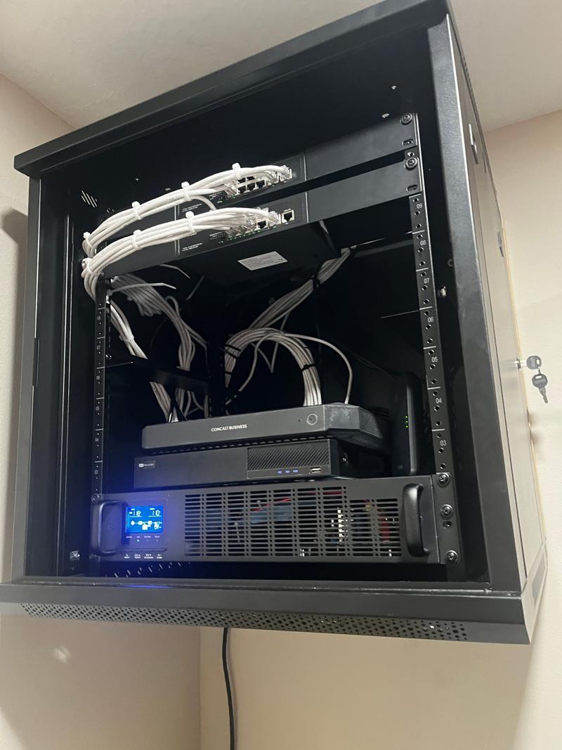 Wall-mounted network rack with PoE switches, recorder, battery backup and neatly bundled Cat6 cabling